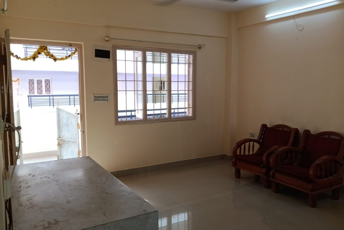 Spacious living room with sofa setup, TV, and natural sunlight in 2BHK flat Electronic City